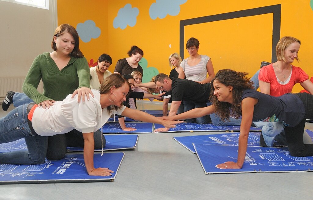 Bewegungslehre: Kursteilnehmerinnen und Teilnehmer führen Bewegungsübungen auf Sportmatten durch